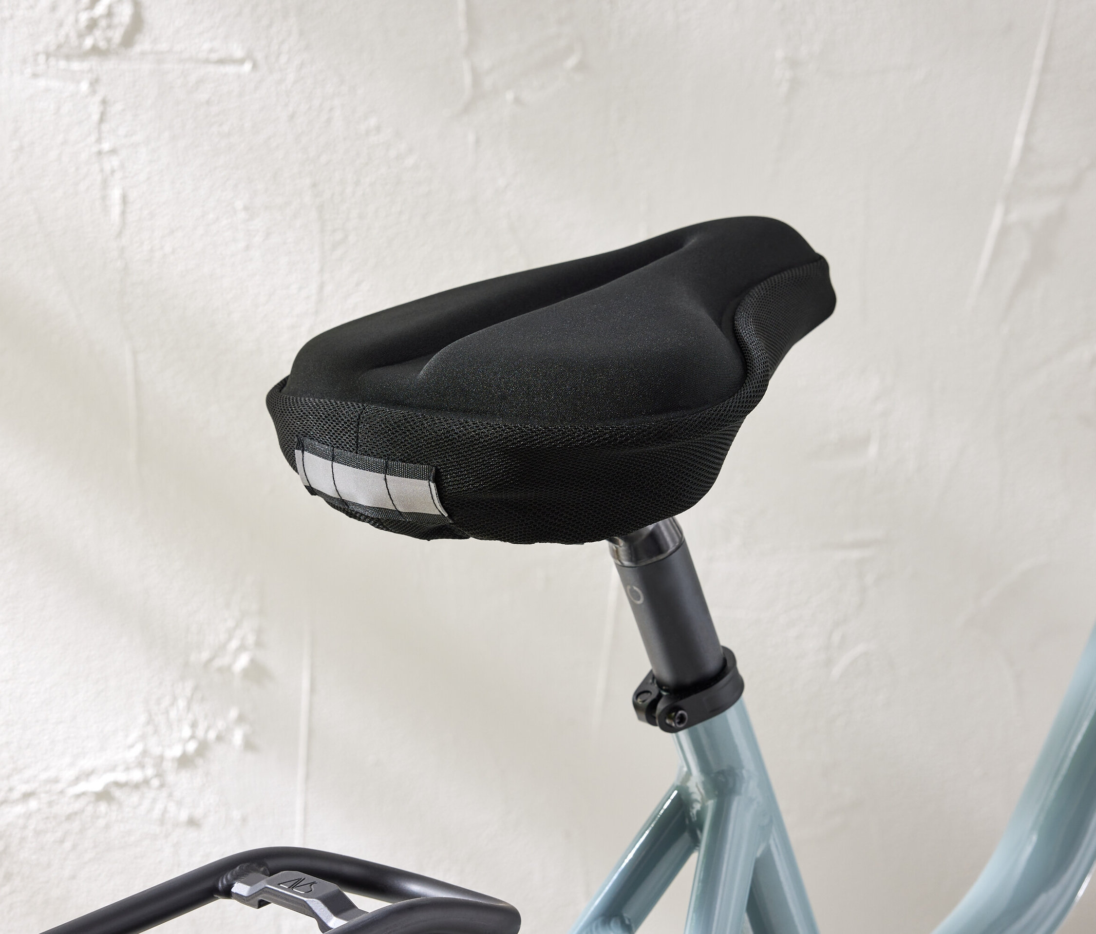 Egy kerékpárülés közeli képe fekete huzattal és fényvisszaverő csíkokkal, fehér fal előtt.