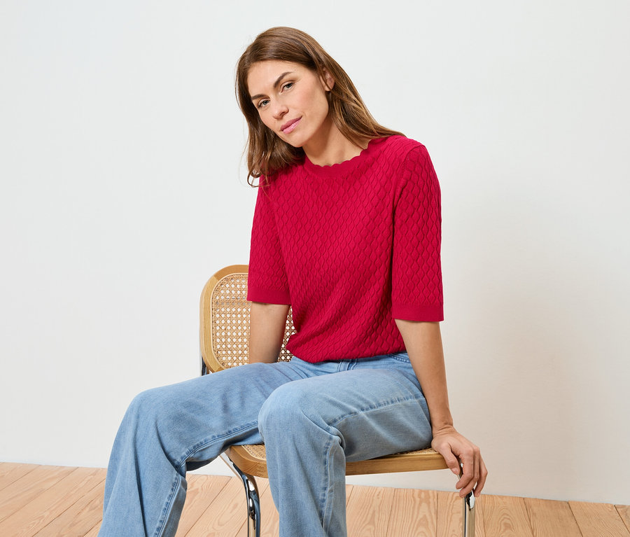 Egy nő ül egy széken, piros felsőben és farmerban.