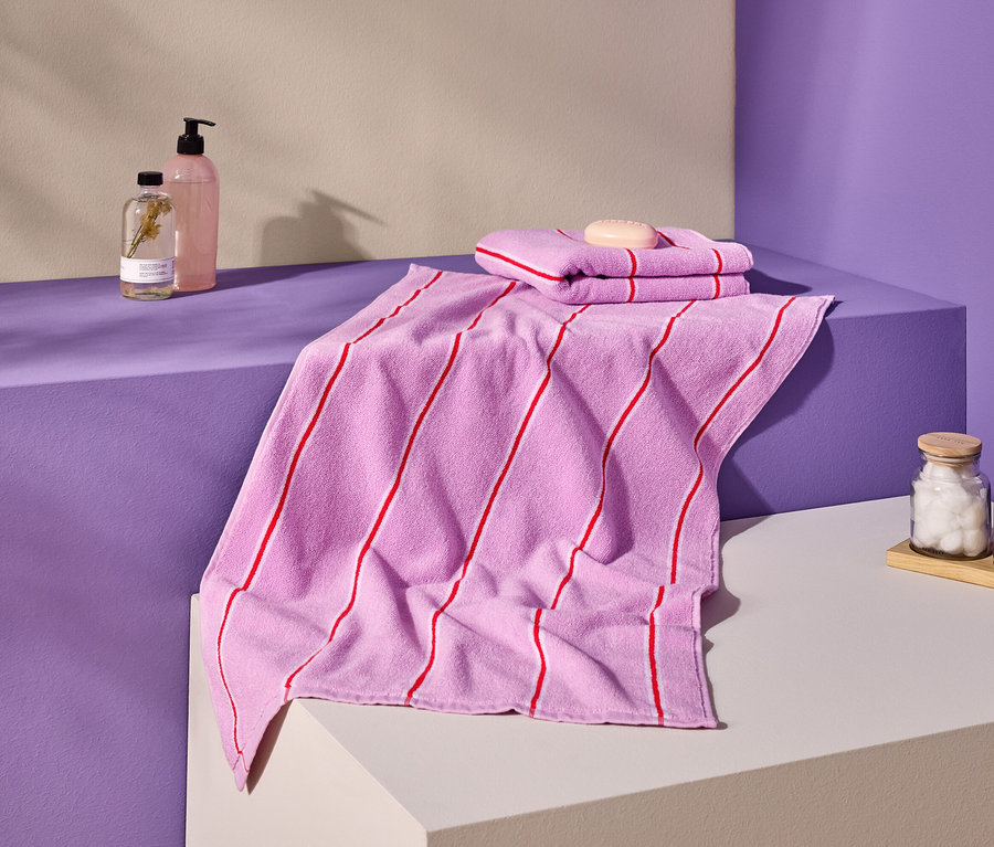 Fotó rózsaszín, piros csíkos törölközőkről, szappanról, üvegekről és tégelyekről lila és krémszínű felületen.