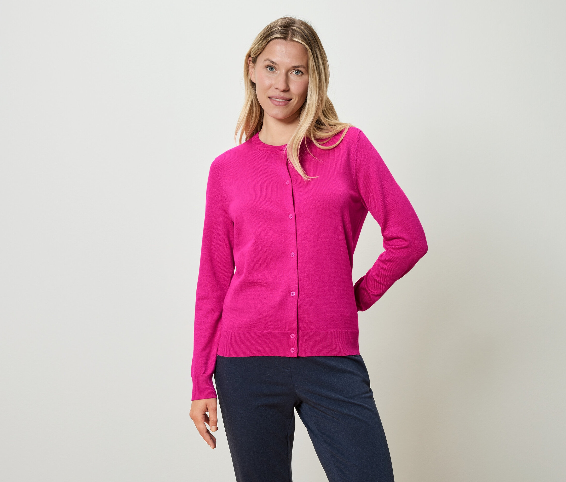 Nő rózsaszín kardigánt és kék nadrágot visel.