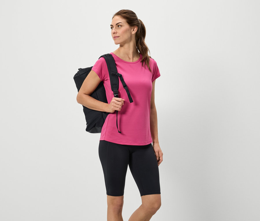 Nő fekete hátizsákkal, rózsaszín pólóval és fekete rövidnadrággal.