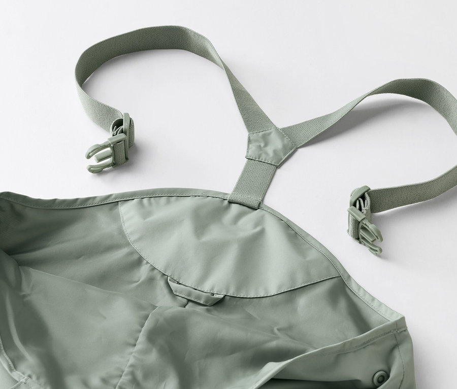 Egy zöld sárnadrág közeli képe, pántokkal és csatokkal fehér háttéren.