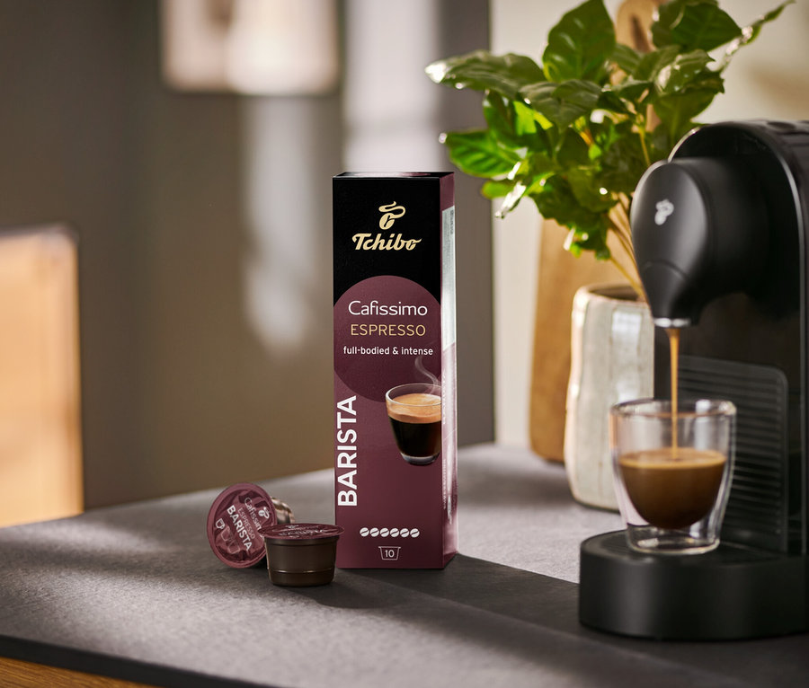 Eszpresszó folyik egy Cafissimo BARISTA kávéfőzőből egy pohárba, mellette egy csomag 10 kávékapszula.