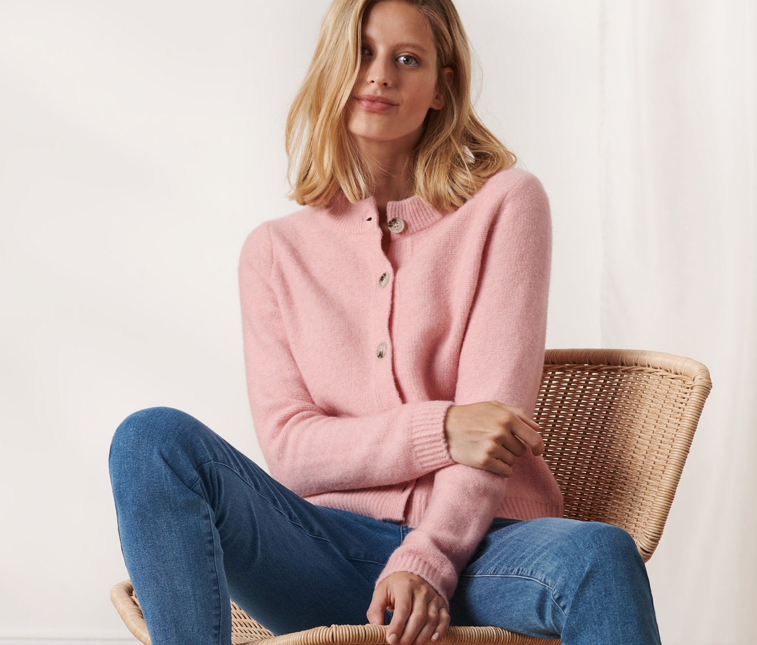 Nő ül egy széken, és rózsaszín kötött kardigánt visel.