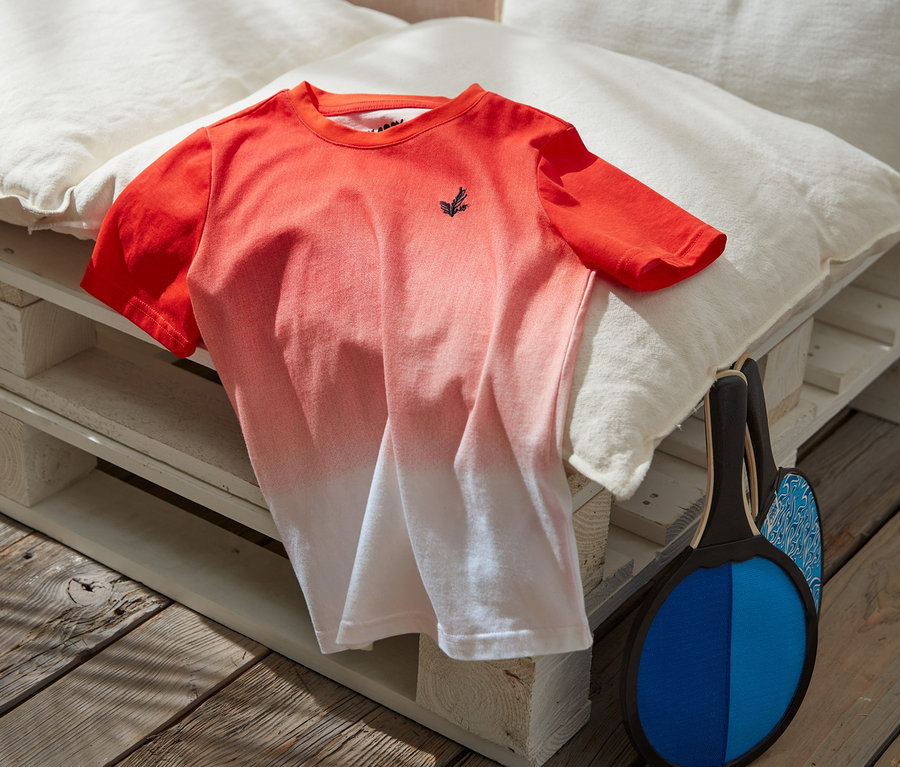 Narancs-fehér fiú póló párnákon fekszik egy strandütő és labda mellett.