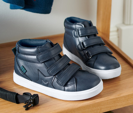 Két sneaker cipő egy fa polcon, alatta kék gördeszka.