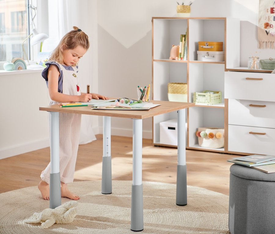 Egy lány rajzol egy Gyerekasztal, állítható magasságú asztalon. A háttérben 2 tárolókosár, egy Tárolókosár és egy Komód, 3 fiókos, furnér hatású élek, fehér látható.