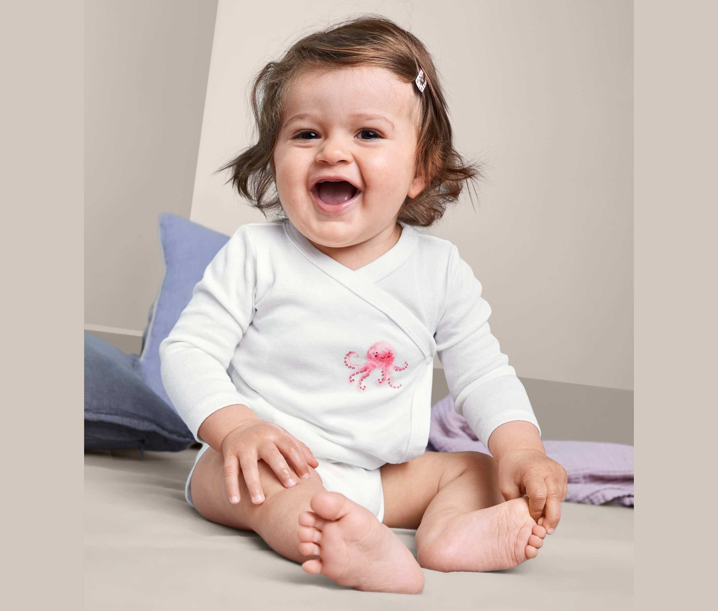 Egy mosolygó baba ül, és egy hosszú ujjú pamut body-t visel, rózsaszín polip mintával.