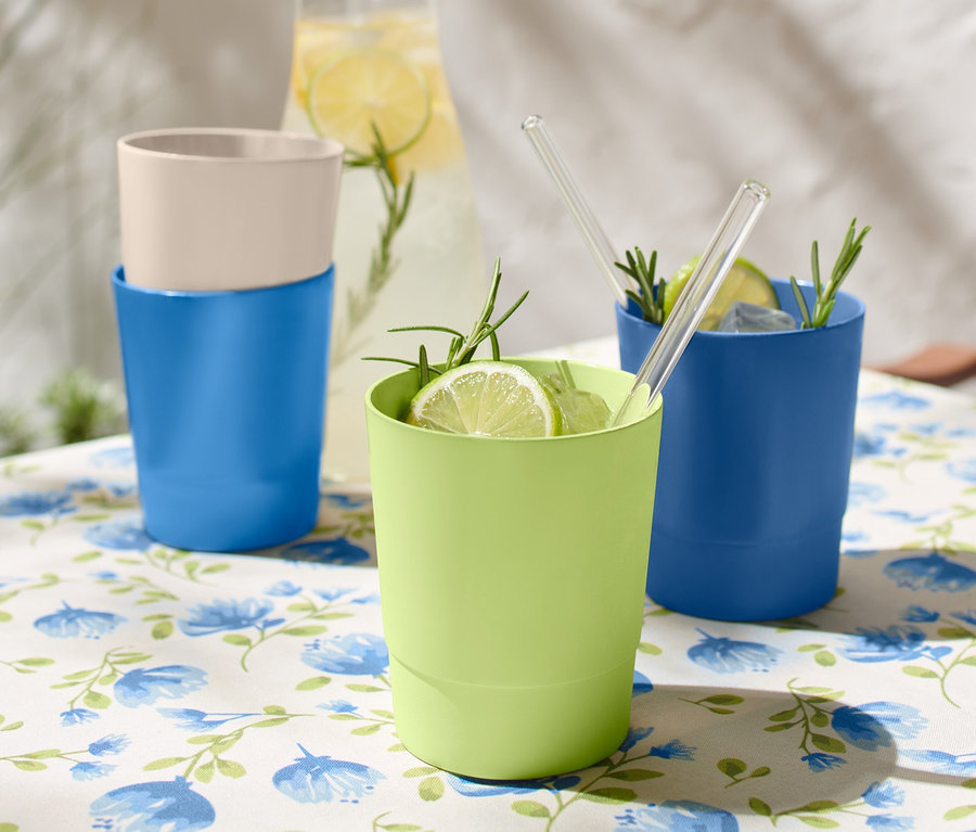 Egy virágos asztalterítővel letakart asztalon 4 műanyag pohár áll, kettő kék, egy zöld és egy bézs színű.