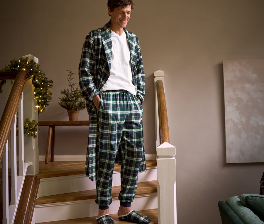 Egy férfi lefelé sétál a lépcsőn kockás flanel köntösben, flanel szabadidőnadrágban, házicipőben és egy V-nyakú pólóban.