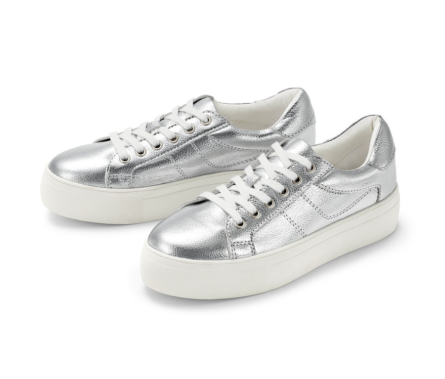 Két ezüst színű, emelt talpú bőr sneaker cipő fekszik egymás mellett fehér háttéren.