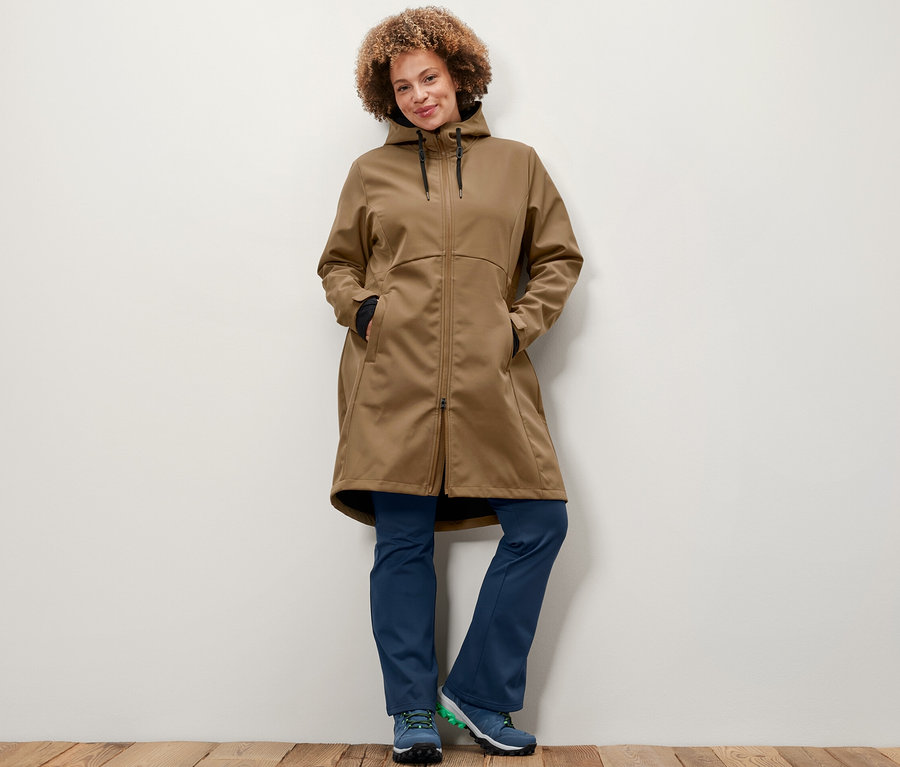 Egy nő pózol nugát színű softshell kabátban és thermo jazzpantsben.