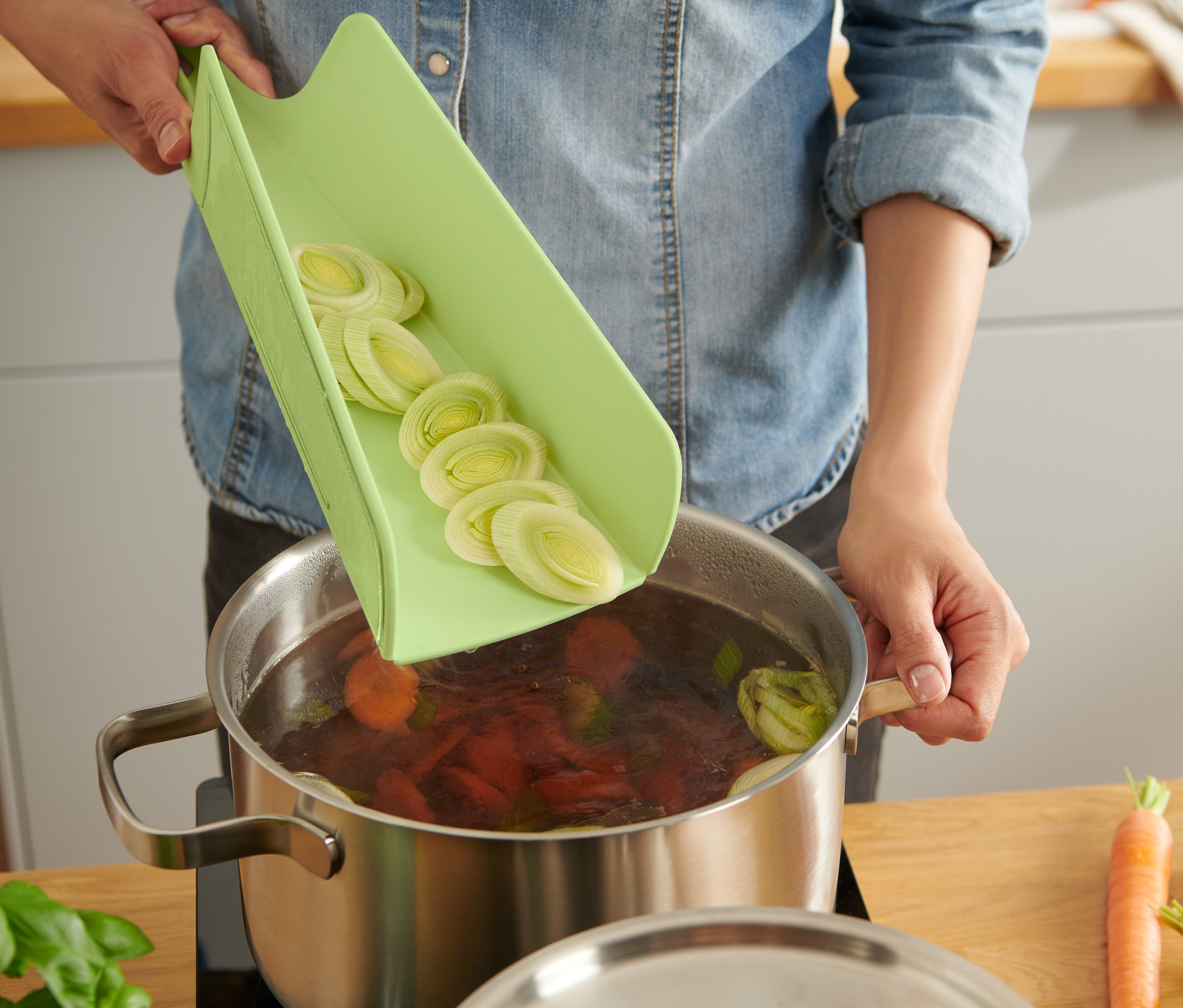 Egy nő felaprított póréhagymát önt egy összecsukható vágódeszkáról egy leveses fazékba.