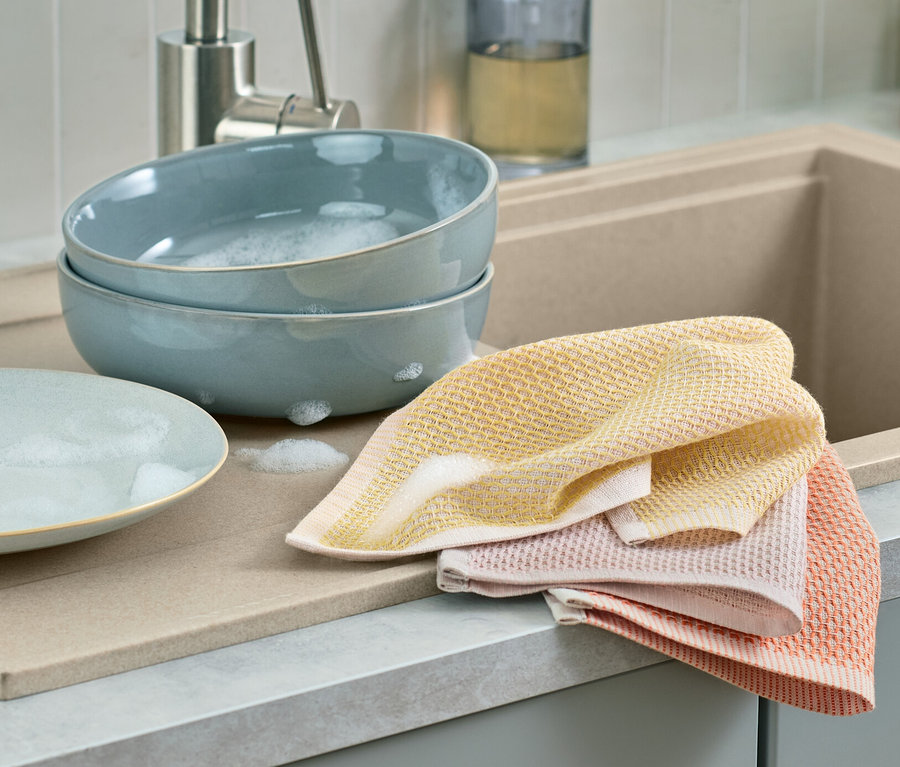 Két kék szappanos vízzel teli tál és egy üres tányér fekszik egymás mellett egy csepegtetőn. Mellettük 3 mosogatókendő található.