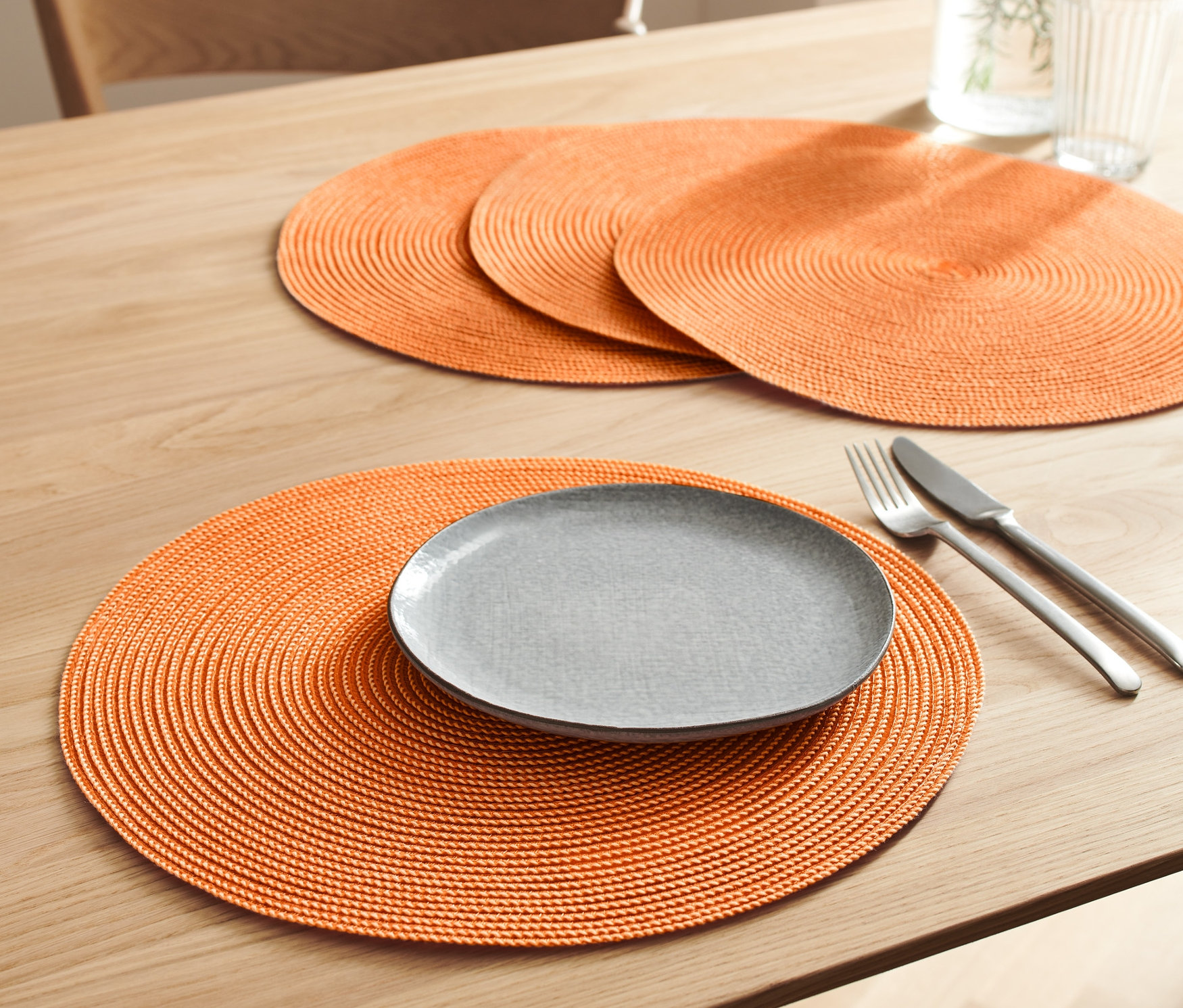 Az asztalon 4 narancssárga tányéralátét található. Az egyiken egy szürke tányér, egy kés és egy villa van.