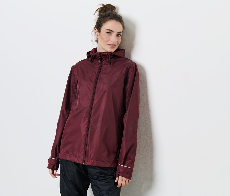 Egy nő a falnak dőlve bordó esőkabátot visel.