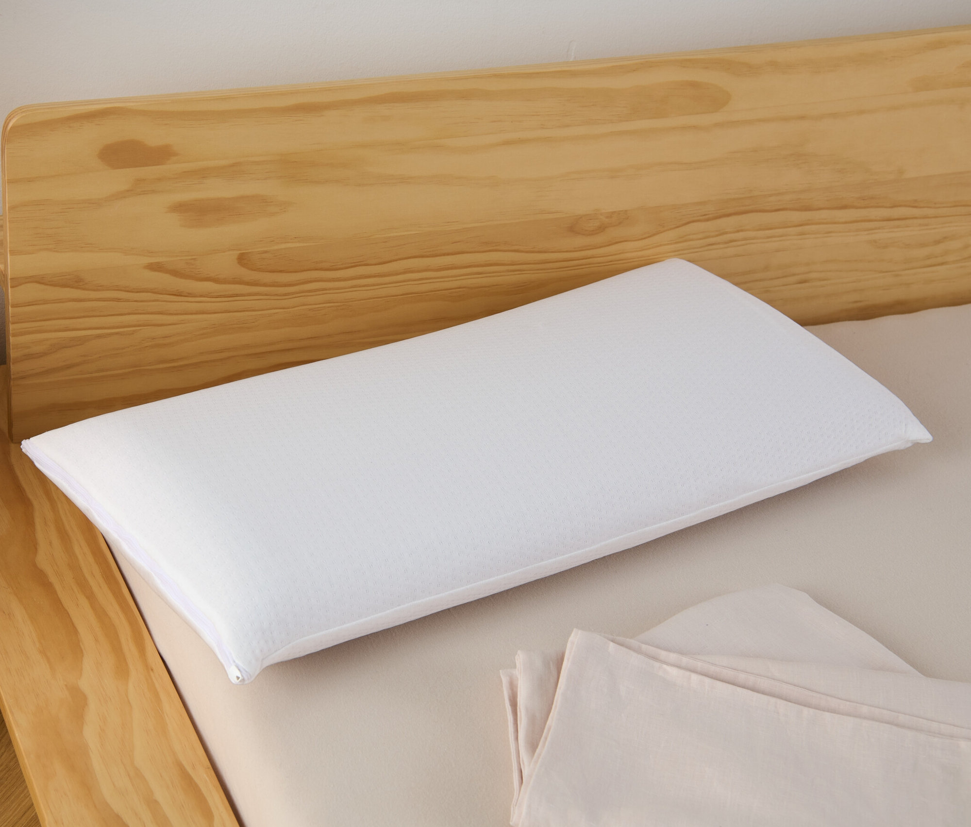 Egy fehér memóriahabos párna fekszik egy fa fejvéggel ellátott ágyon.