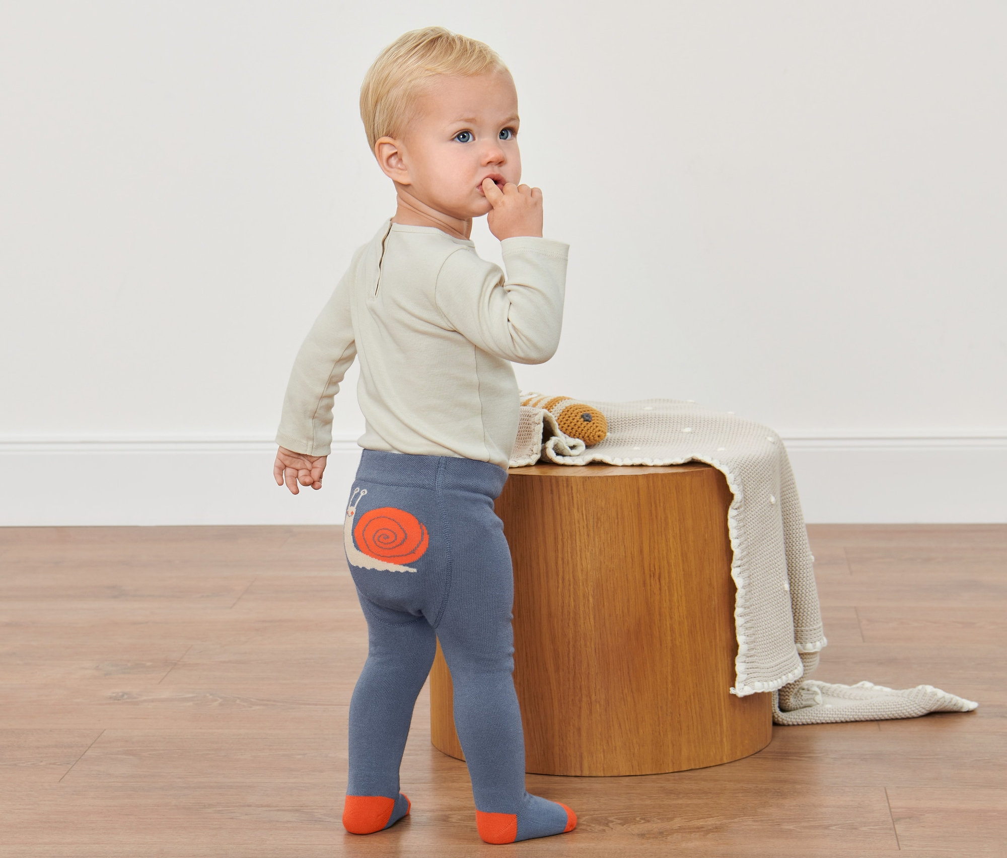 Kisgyermek áll a padlón, csigamintás harisnyát visel.
