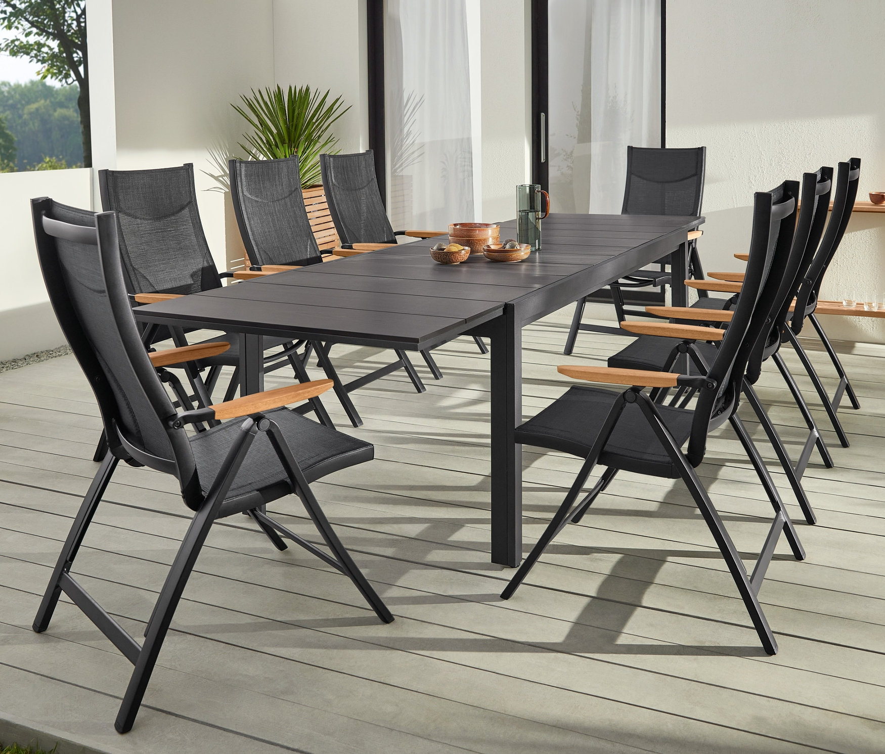 Fekete, Duraboard anyagból készült kihúzható asztal két kültéri LED-es asztali lámpával és magas támlájú székekkel.