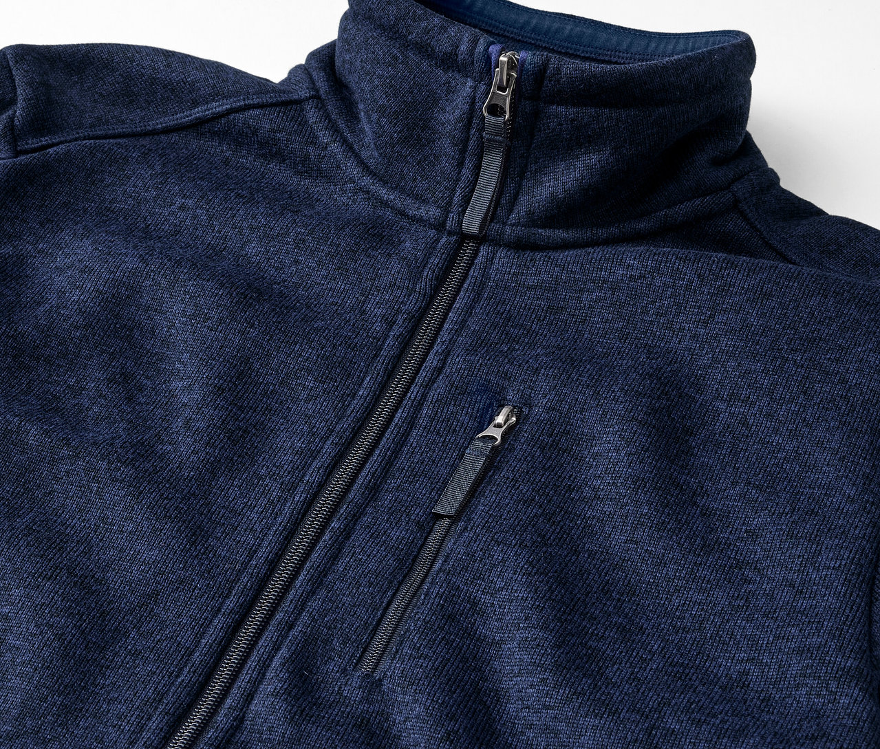 Egy sötétkék, kötött polár felső részlete cipzárral.