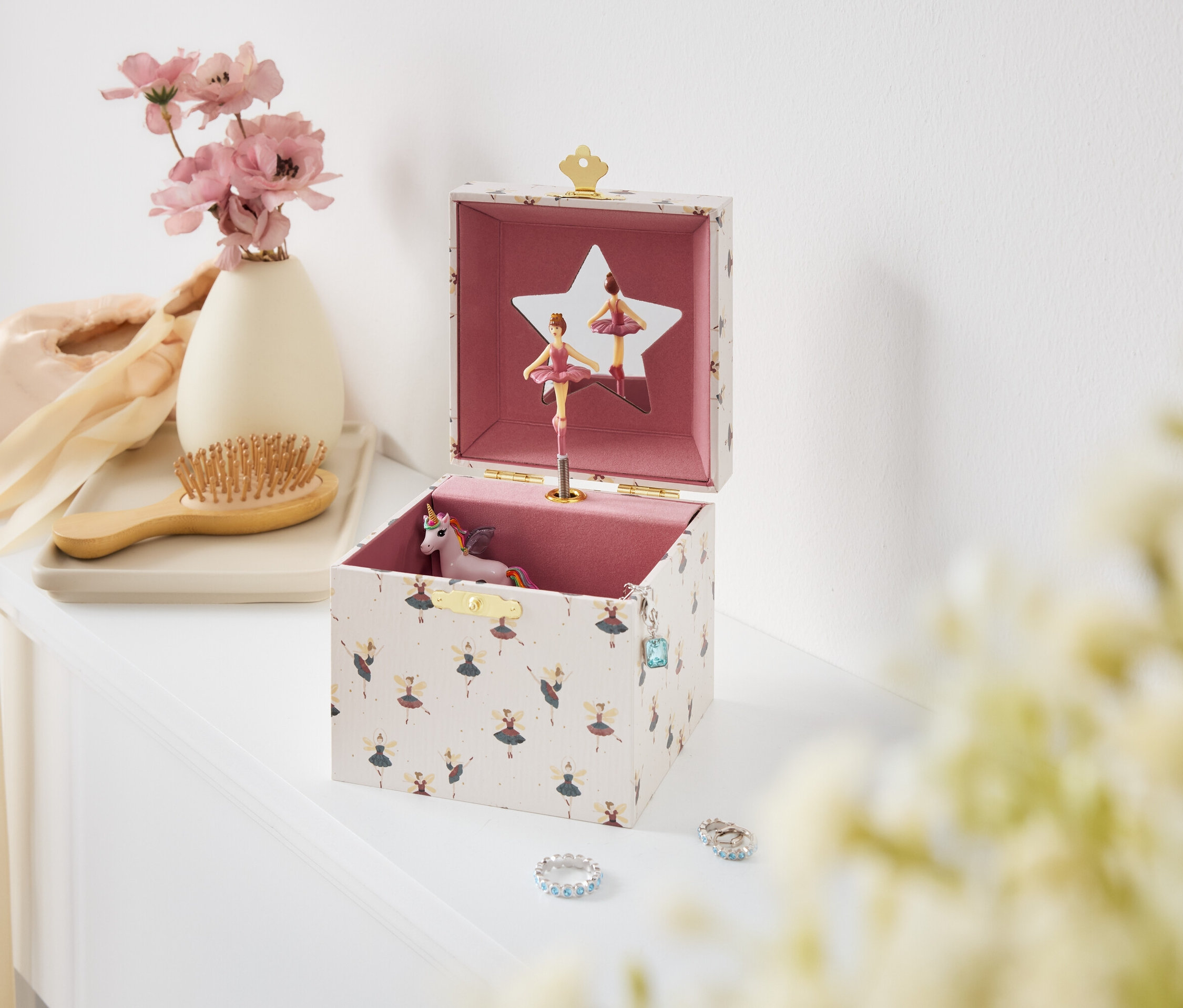 Nyitott zenélő doboz balerinákkal és unikornissal egy fehér asztalon.