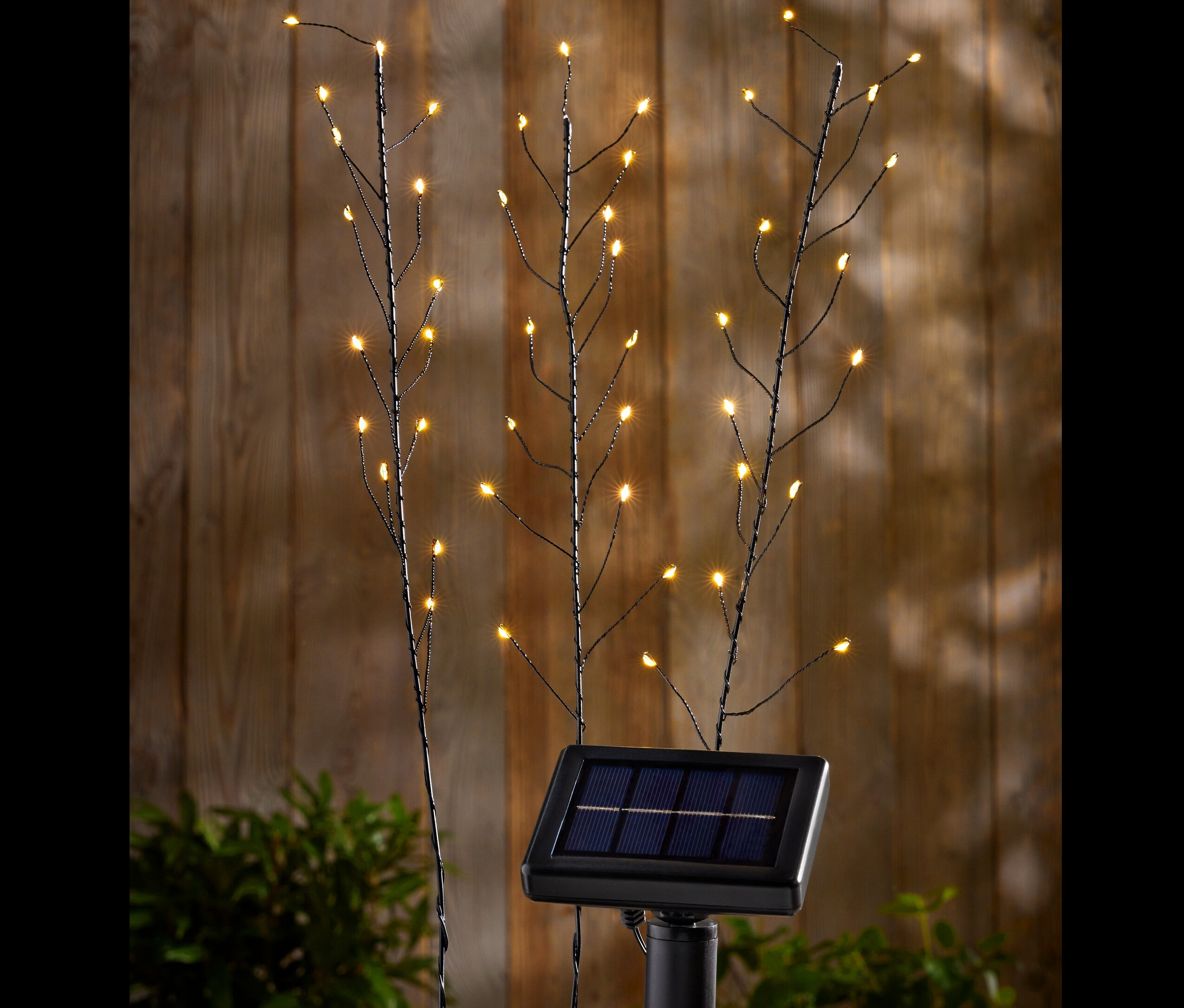 Három szolárnyárs LED-es lámpákkal egy fa fal előtt.