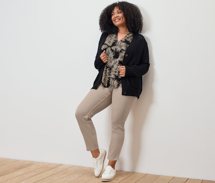 Nő pózol 7/8-os treggingsben, felsőben és kardigánban.