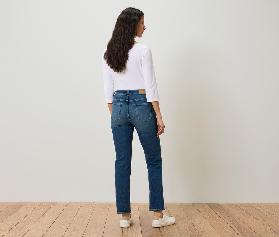 Egy nő áll háttal, kék farmerben, fehér ingben és fehér tornacipőben.