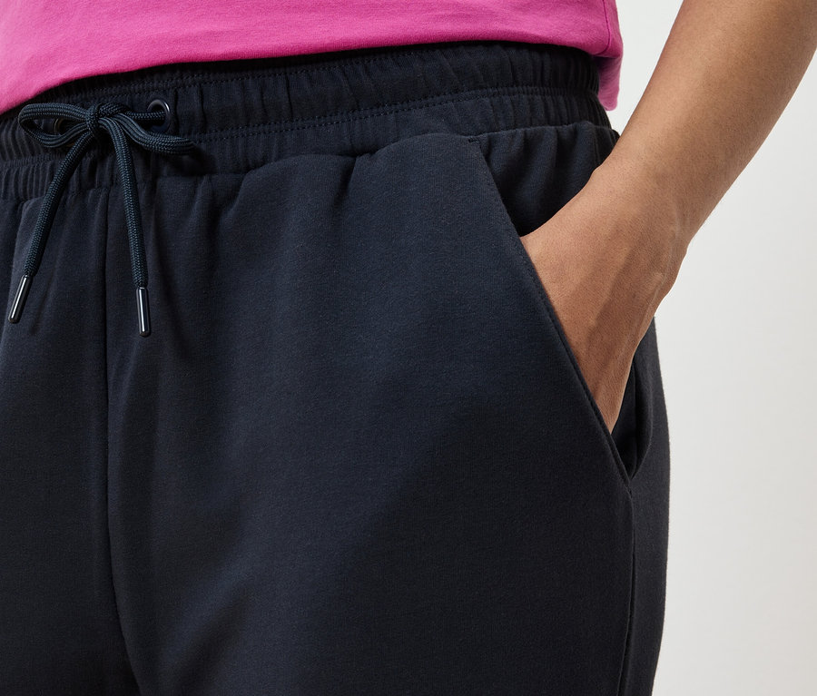 Egy sötétkék melegítő alsó részletképe, kézzel a zsebben és egy rózsaszín pólóval.