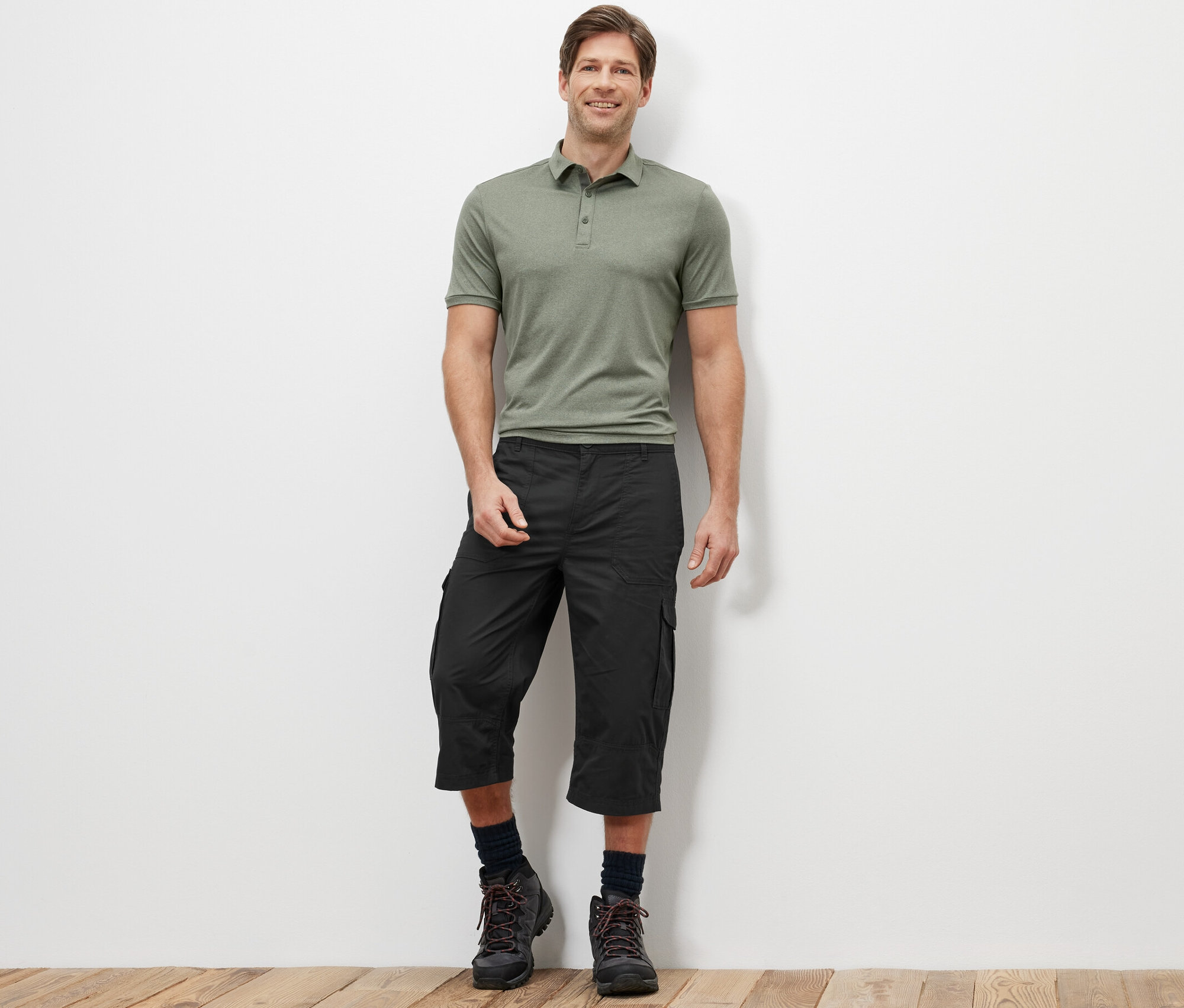 Egy férfi áll zöld pólóban és antracit színű, 3/4-es cargo bermudában.