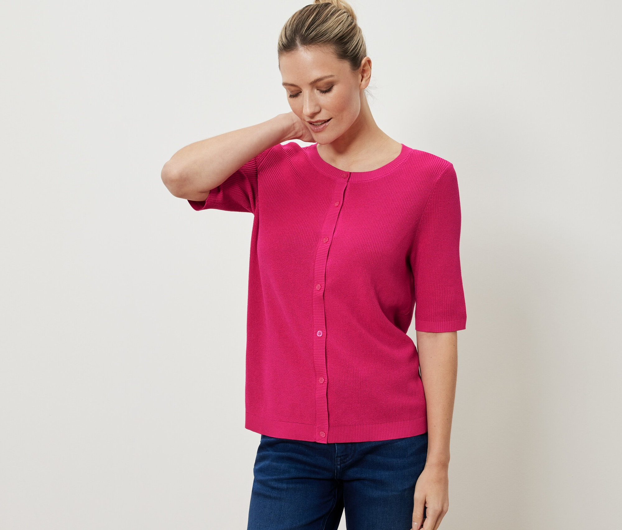 Nő visel rózsaszín finomkötésű, lenvászon kardigánt és farmert.