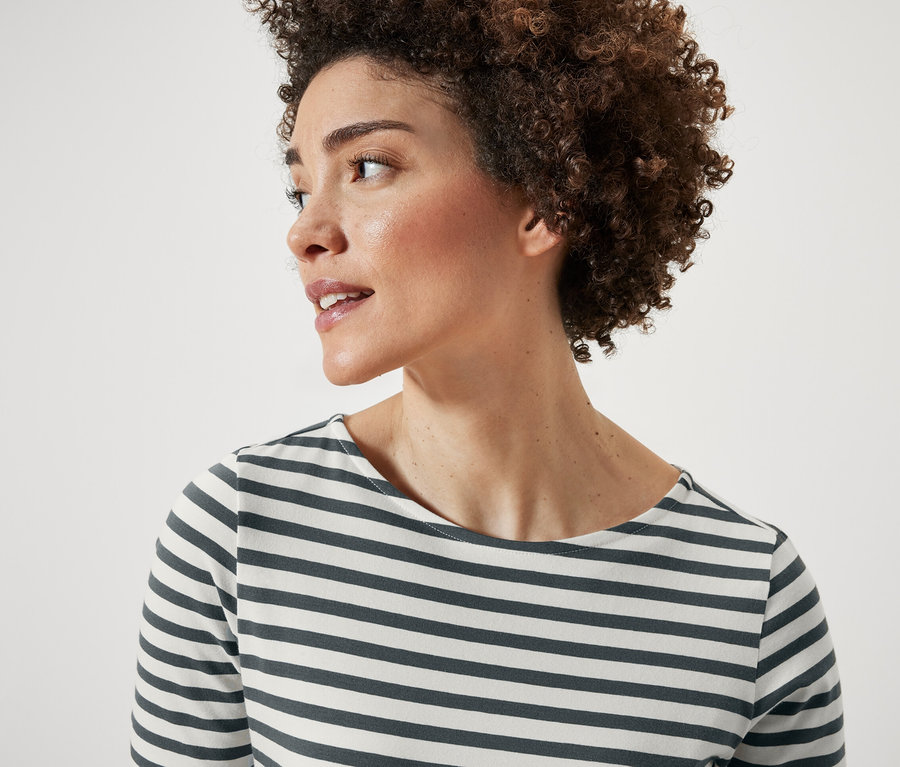 Portré egy rövid, göndör hajú nőről. Zöld csíkos, félhosszú ujjú felsőt visel.