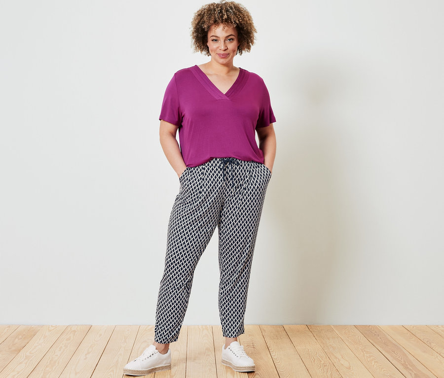 Nő pózol Női V-nyakú felső fukszia színben és Női jersey nadrág, mintás, sötétkék színben.