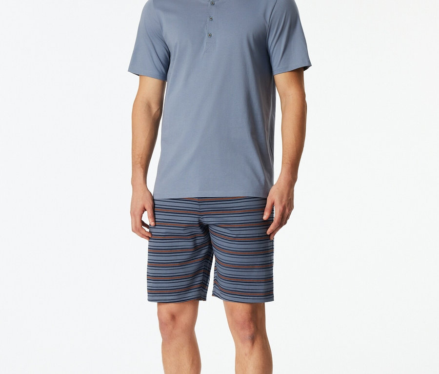 Férfi kék, gombos pizsama felsőben és csíkos rövidnadrágban.