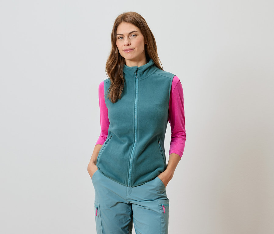 Nő petrolmellényben, hozzáillő nadrágban és rózsaszín hosszú ujjú felsőben.