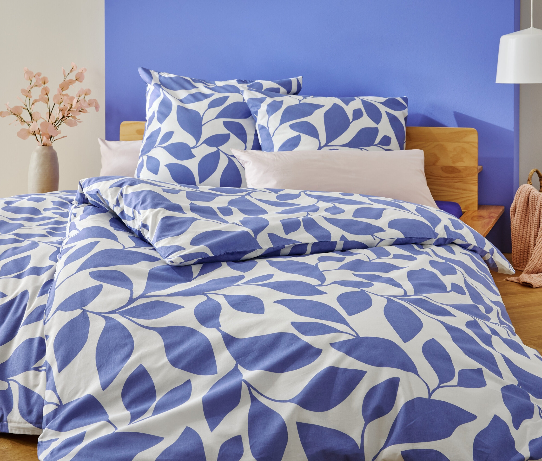 Egy ágy kék-fehér levélmintás ágyneművel, a kékre és fehérre festett fal előtt.