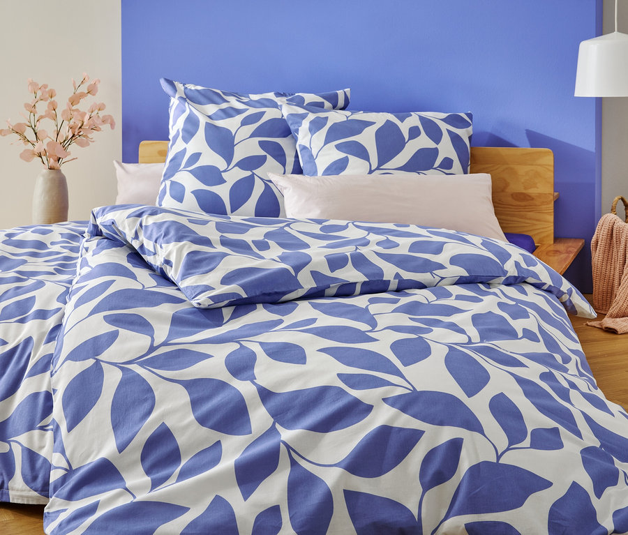 Egy ágy kék-fehér levélmintás ágyneművel, a kékre és fehérre festett fal előtt.