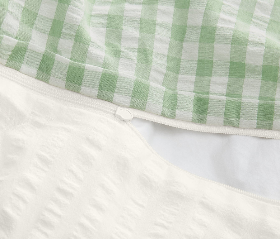 Egy részben kinyitott, cipzáras paplanhuzat közeli képe, a teteje zöld-fehér kockás, az alja texturált fehér.