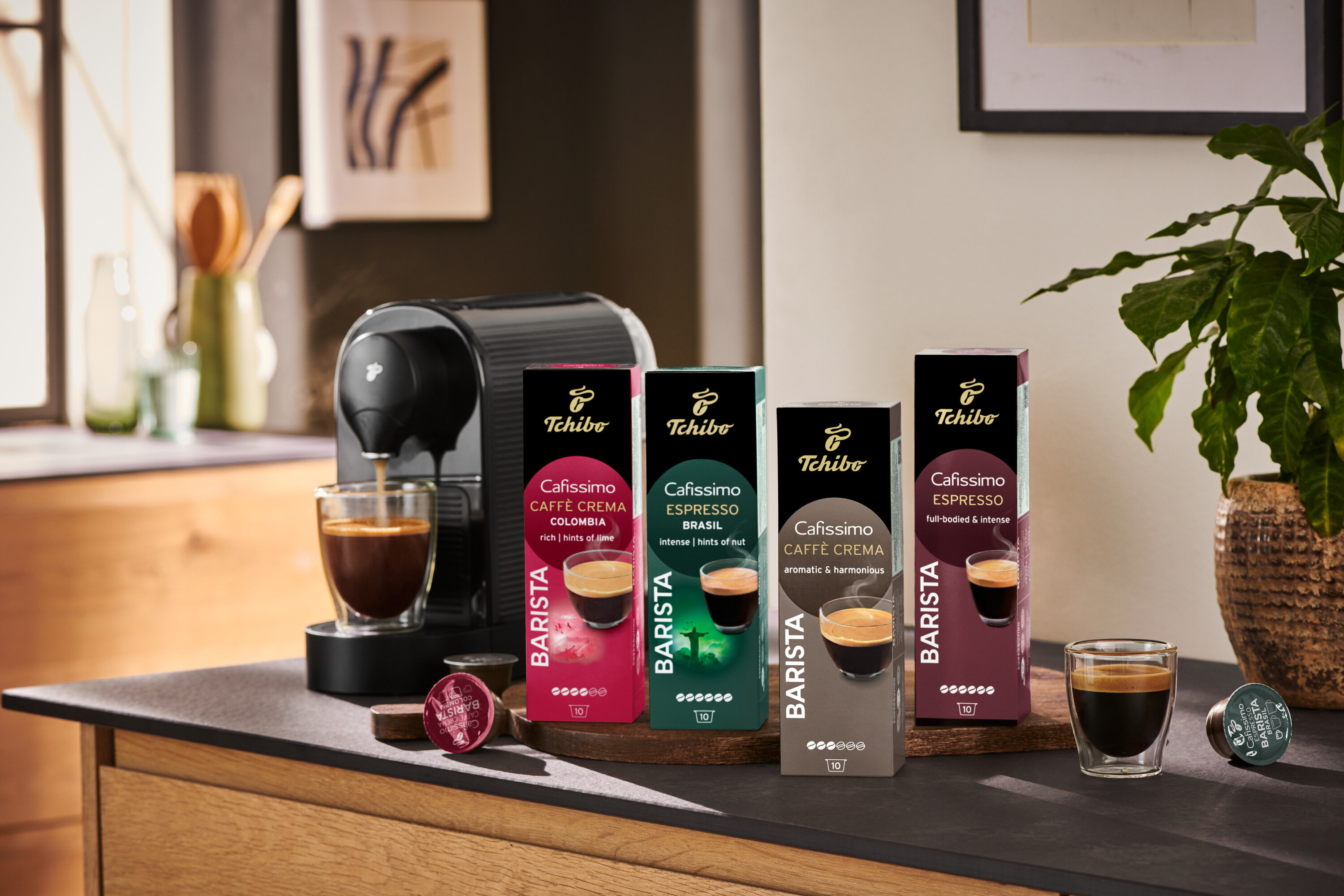 Kávéfőző kávéval tölti a poharat a Cafissimo Barista Edition Espresso – 80 db kávékapszula csomagolásai mellett.