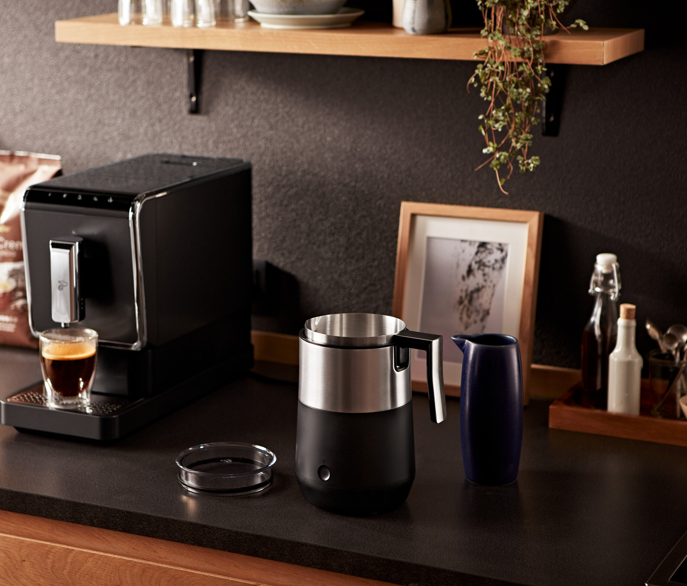 Az eszpresszógép kávét tölt egy pohárba egy fekete indukciós tejhabosító mellett.