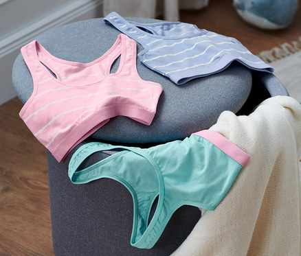 Három bio pamut bustier melltartó egy szürke puffon.