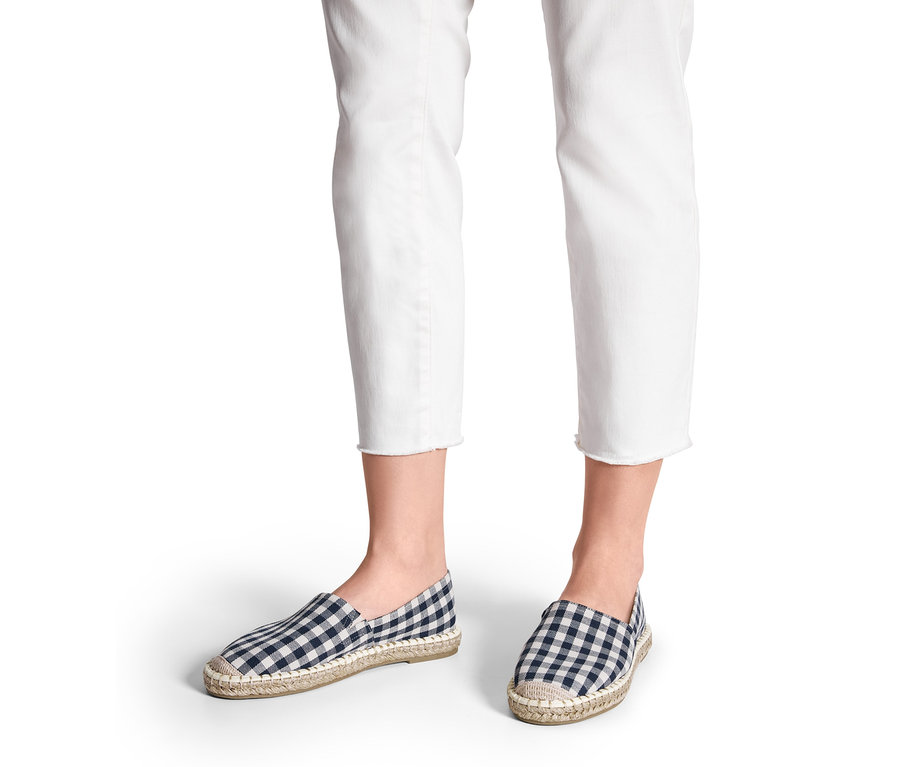 Fehér farmerben lábak, sötétkék/fehér kockás női espadrilles cipőben.