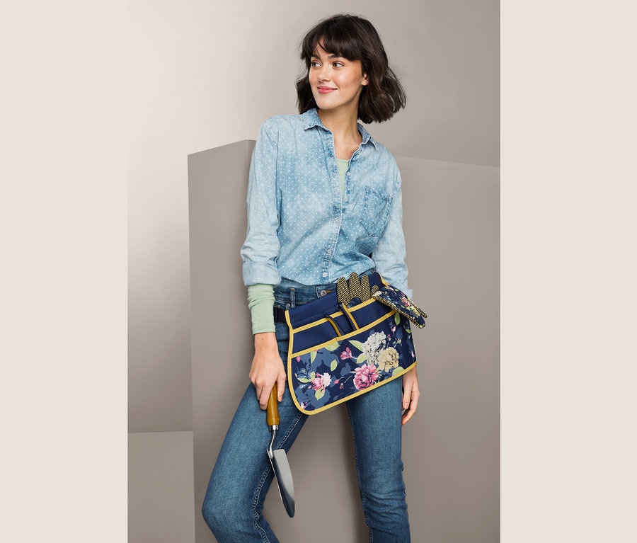 Nő virágos kerti szerszámtartó övet visel és kerti ásót tart.