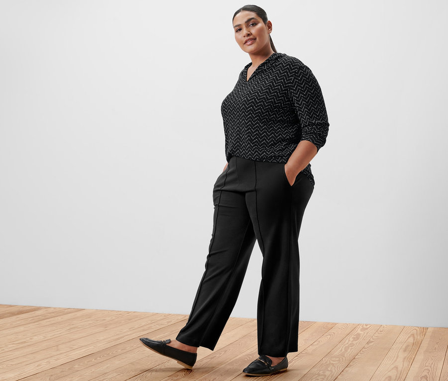 Nő pózol fekete nadrágban és nyomtatott mintás, V-nyakkivágású hosszú ujjú felsőben.