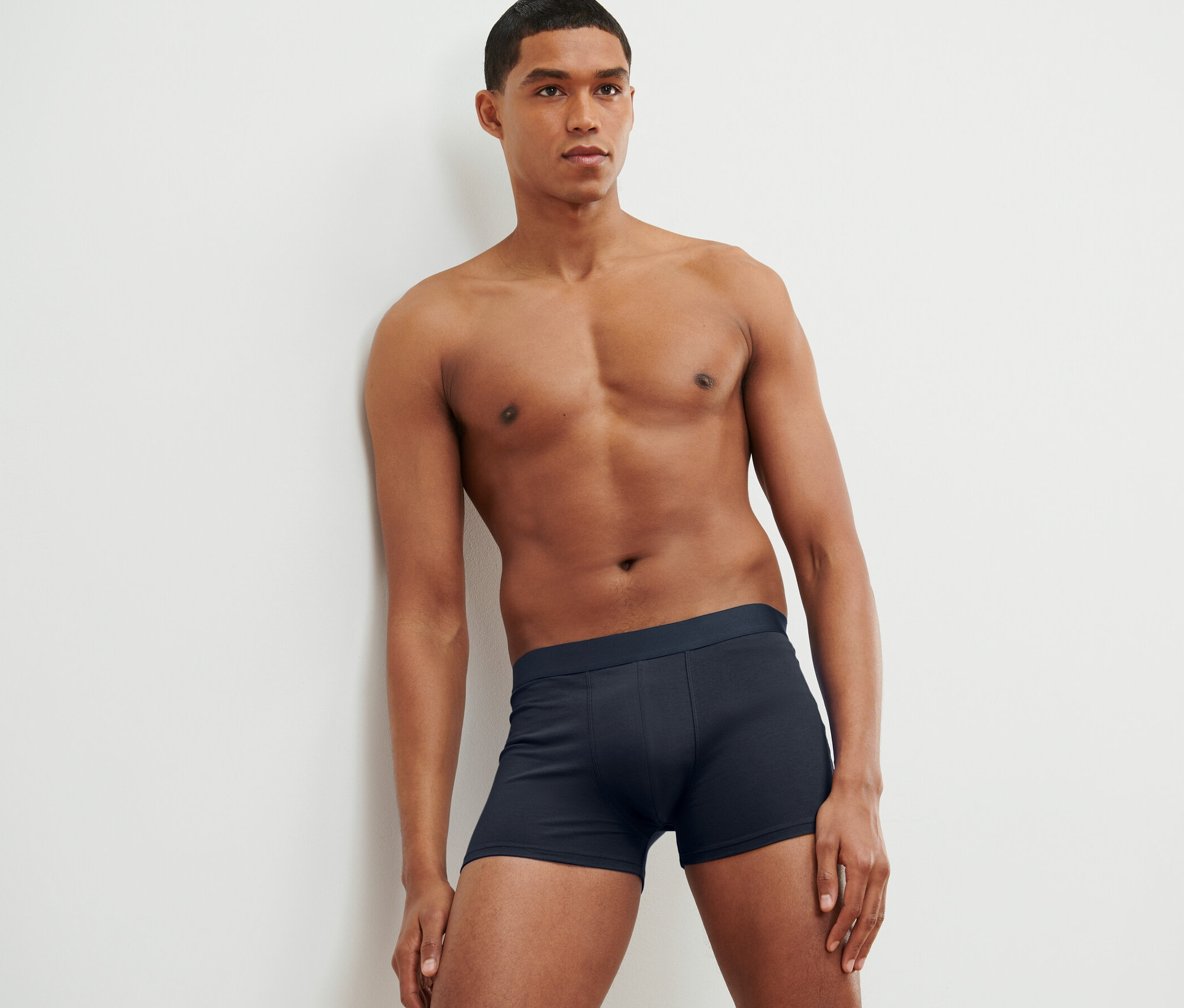 Férfi a falnak támaszkodva, 4 db-os sötétkék férfi boxer alsónadrágot visel.