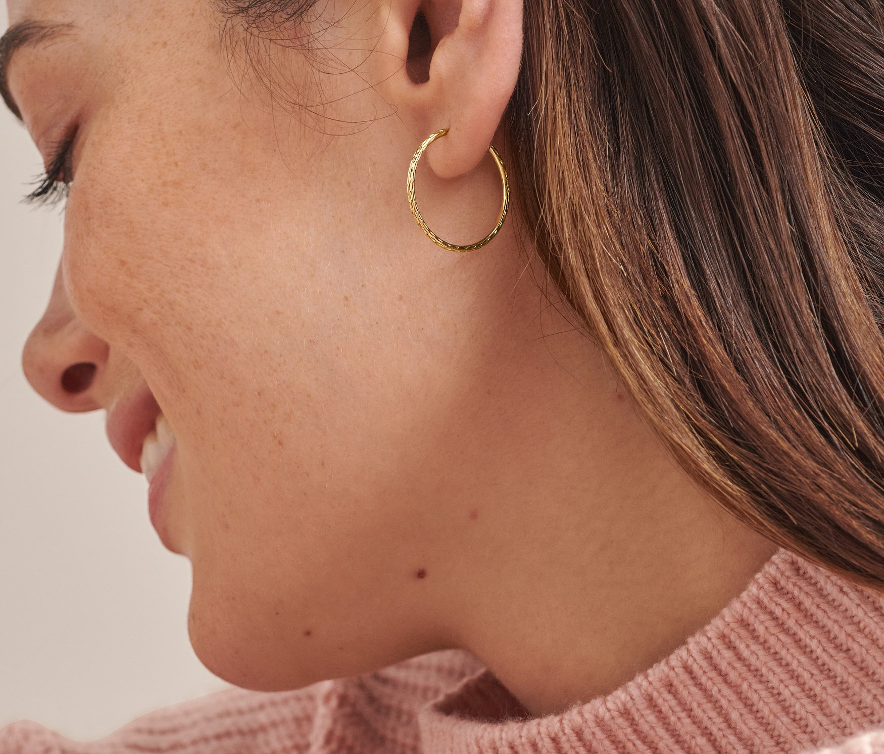 Egy nő arcának közeli képe, aki Női arany karika fülbevalót, Basic, flexibilis fülbevalót visel.