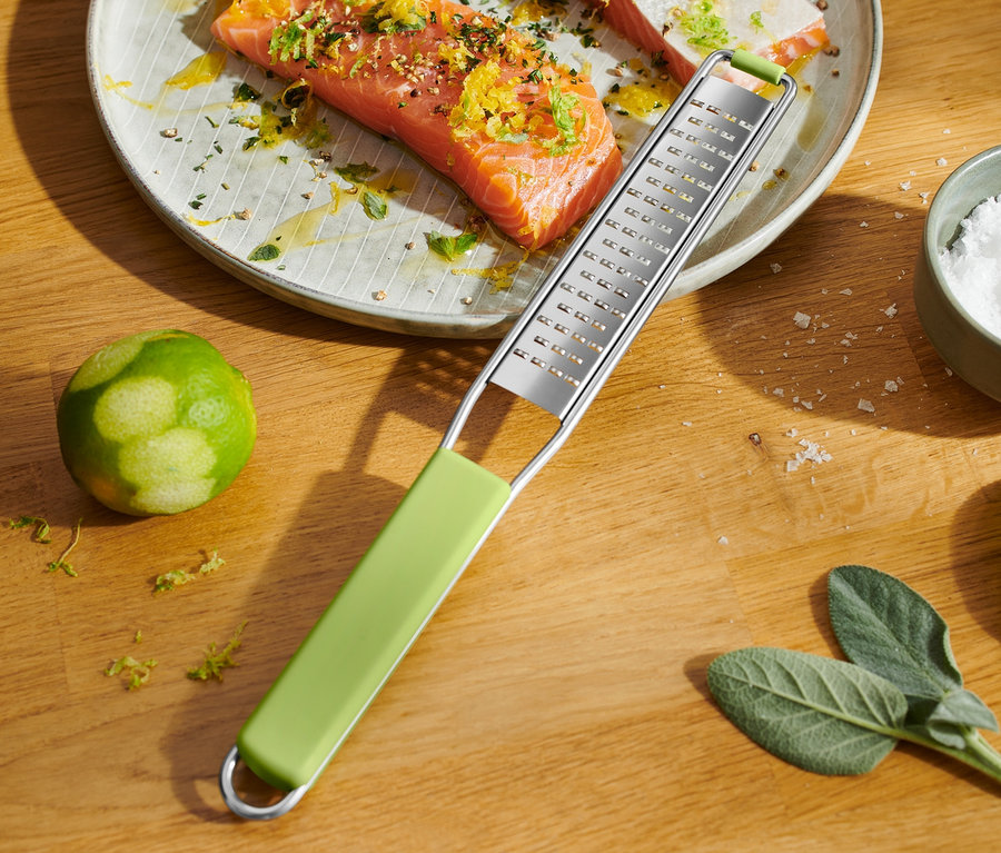 Citruskérgekkel megszórt lazac egy tányéron. Mellette egy finom kézi reszelő.