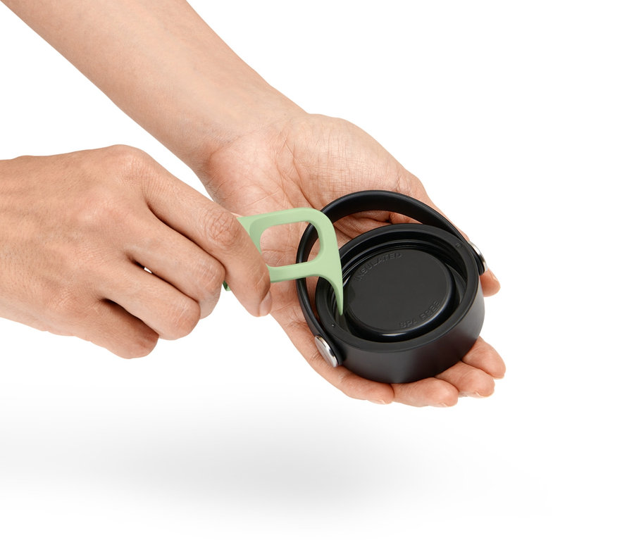 Kezek egy zöld eszközzel tisztítják a menetet egy palack kupakján.