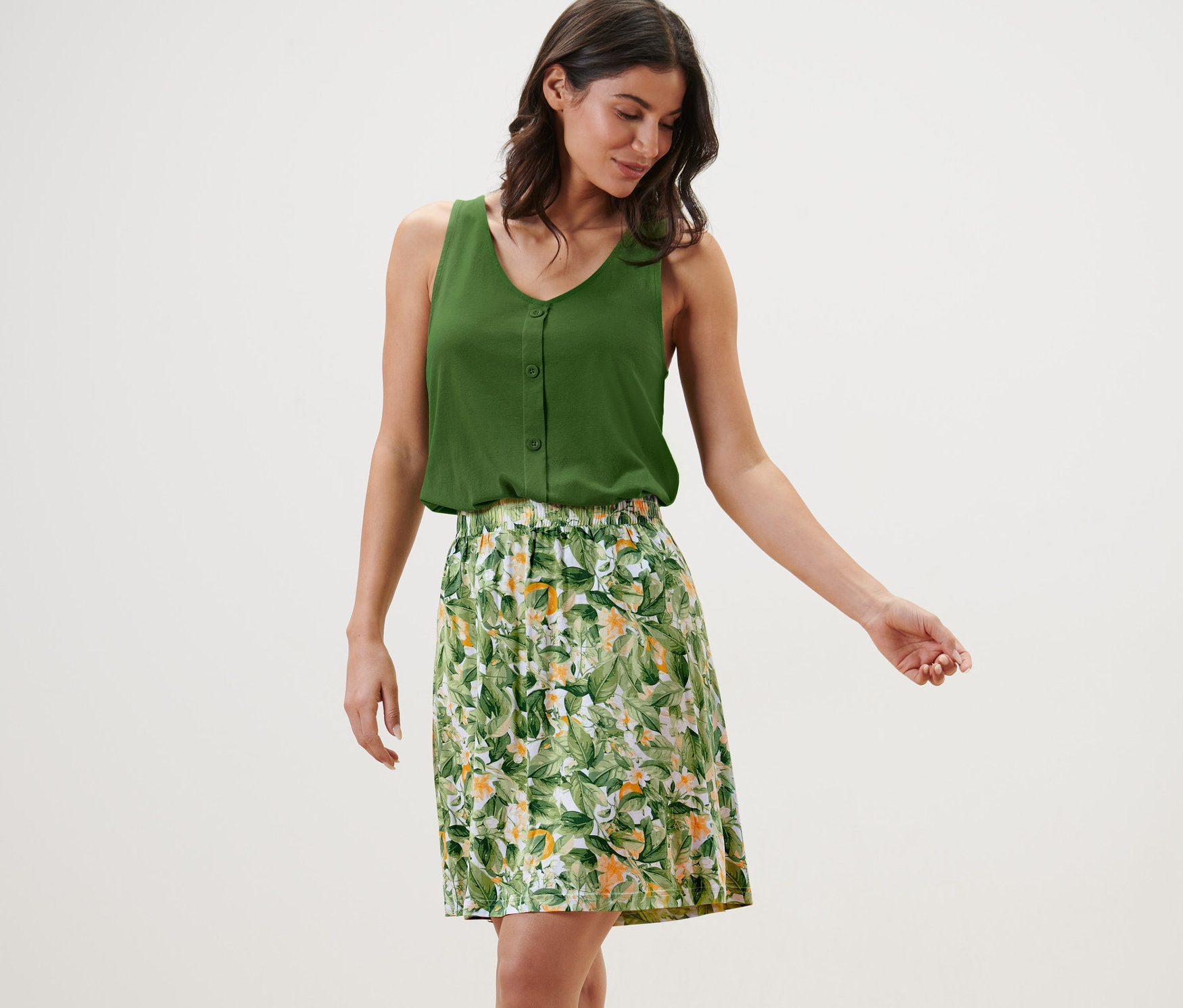 Nő visel egy zöld felsőt és egy nyomott mintás jerseyszoknyát.