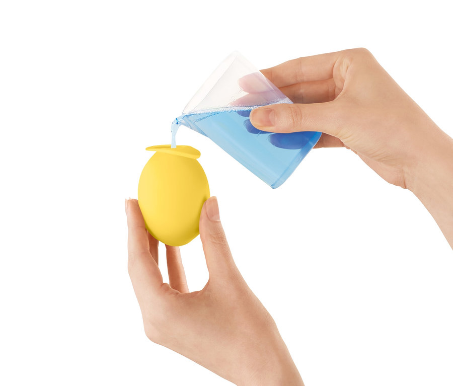 Egy nő kék folyadékot önt egy mérőpohárból egy sárga vízkőmentesítő fej vízcsapra.